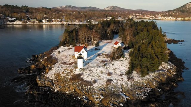 Low and Slow aerial fly over of snow covered Curtis Island Lighthouse at sunrise with long shadows in the snow