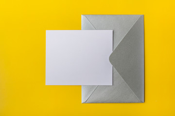 Mock-up letter or card with a silver envelope on a yellow background. Copy space. View from above