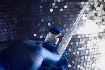 Close-up Of A Doctor's Hand in blue medical gloves holding syringe and vaccine.