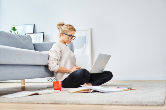Young woman sitting on floor at home working with laptop and documents