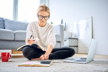 Young woman paying bills online and managing home finance while sitting on floor