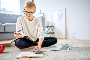 Young woman sitting on floor at home managing home finances