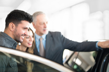 Happy young family talking to the salesman and choosing their new car in a showroom