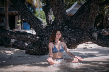 Young slim girl sitting in the shade of a tree in the sea waves on the coast of a tropical island