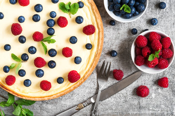 Classic New York cheesecake with fresh berries, mint and cutlery on stone background, top view