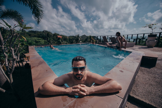 Portrait of a young handsome man in an outdoor pool. Attractive guy with a beard at the side of the pool