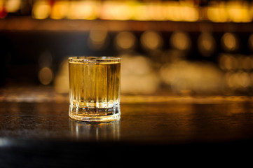 Glass filled with strong cocktail with light whiskey on the bar against the lights