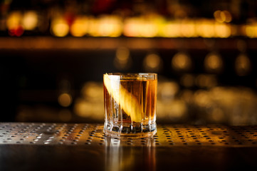 Elegant low glass filled with strong cocktail with light whiskey on the bar against the golden lights