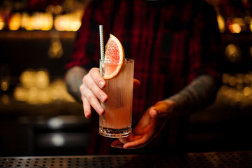 Bartender holding a glass of fresh and sour fruit alcoholic cocktail with grapefruit