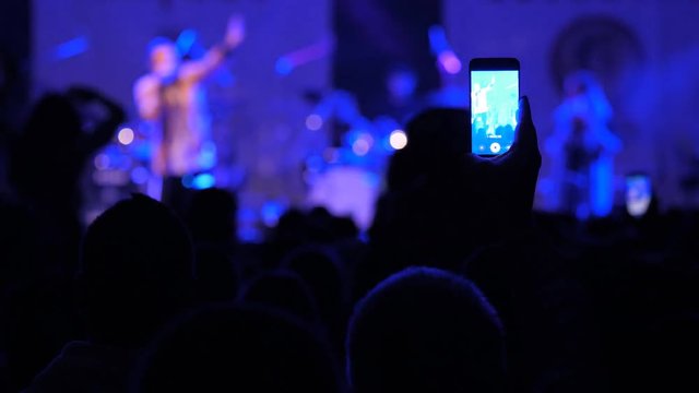 People with smart phones take photos of the artist on stage during concert