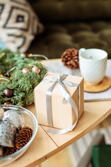 Christmas gift in a beautiful paper box on a small wooden table with Christmas decor.