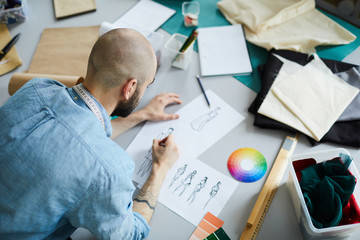 Overview of young creative fashion designer leaning over sketch of new models