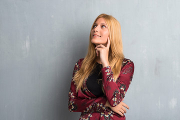 Blonde woman standing and thinking an idea on textured wall background