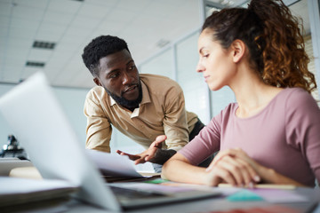 Confident young designer explaining something in paper to his colleague at meeting