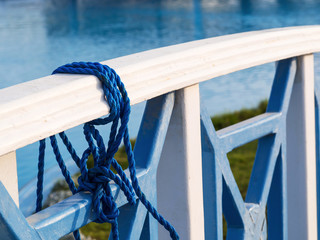 Blue twisted rope tied on the wooden bridge railing near the lake, closeup © yurich84