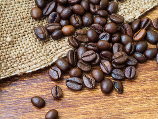 Heap of roasted coffee beans on bagging and wooden background, macro