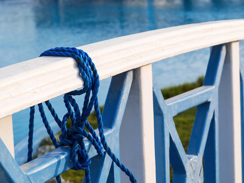 Blue twisted rope tied on the wooden bridge railing near the lake, closeup