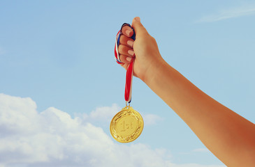 Plakat woman hand raised, holding gold medal against sky. award and victory concept.