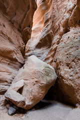 A huge boulder lies in the bottom of a deep slot canyon underheath a canyon wall reflecting sunlight from above at Kasha-Katuwe Tent Rocks National Monument