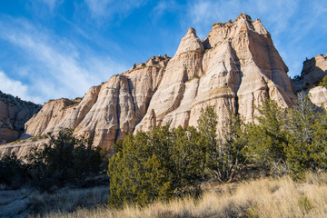 Fototapeta premium Steep, eroded rock formation with multiple sharp peaks under a blue sky with wispy clouds at Kasha-Katuwe Tent Rocks National Monument, New Mexico