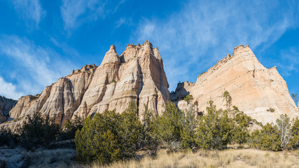 Panorama of steep, sharp peaks and rock formations over a grassy meadow under a blue sky with wispy clouds at Kasha-Katuwe Tent Rocks National Monument