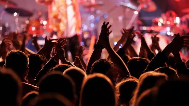 Night concert crowd raise and clap their hands in front of stage lights