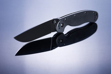 Folding knife and its reflection in the glass. Knife in the center of the table.