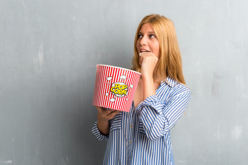 Blonde girl eating popcorns in a big bowl on textured grunge wall background