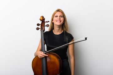 Young blonde girl with her cello posing on white wall
