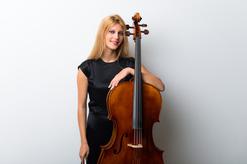 Young blonde girl with her cello posing on white wall