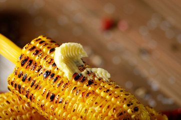 Deep grilled sweet corn cob under melting butter on plastic holder
