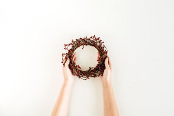 Wreath frame made of red berries in female hands on white background. Flat lay, top view Christmas / New Year festive mock up blog hero header.