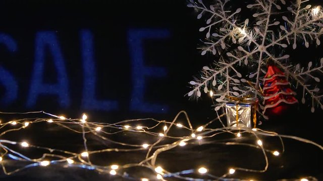 Christmas sale concept for store showcase windows. with word sale flashing on dark background. white garland, big snowflake and small gift box as decorations
