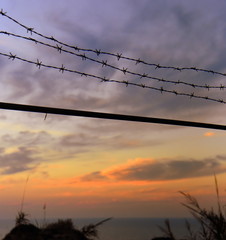 Farbenprächtiger Sonnenuntergang am Meer mit Stacheldrahtzaun 