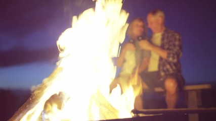 Carefree retired Caucasian American couple enjoying camping sitting by the campfire toasting with red wine at the night 