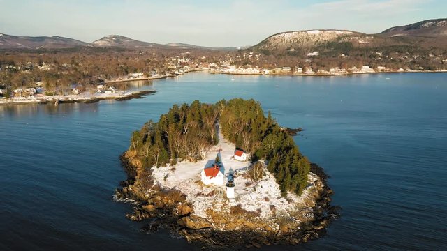 Aerial flyby and tilt down over snow covered Curtis Island Lighthouse at sunrise with long shadows in the snow