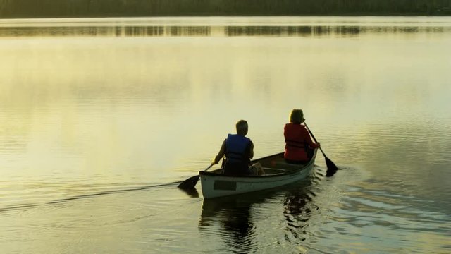 Silhouette of mature Caucasian American couple enjoying leisure on the kayaking trip at sunrise on the lake outdoors 