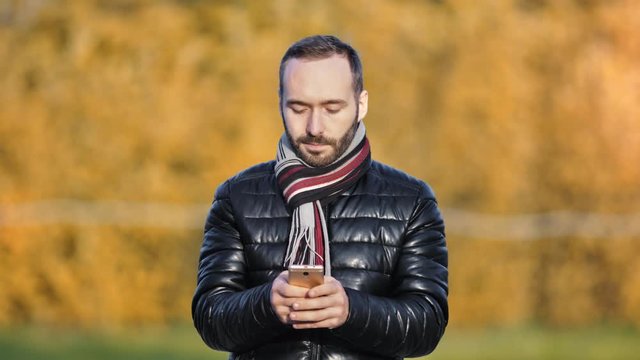 Fashion European man typing message using smartphone at autumn evening in cold weather