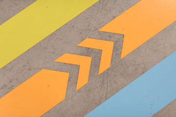 a orange arrow road sign inside basement car park. the arrow road sign at floor, it point to an empty carpark slot. Yellow and blue lines
