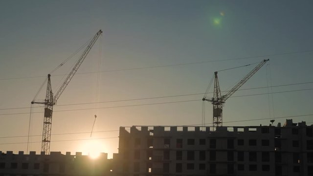 Crane and building construction site at sunset. Silhouette workers on a background of the sky.