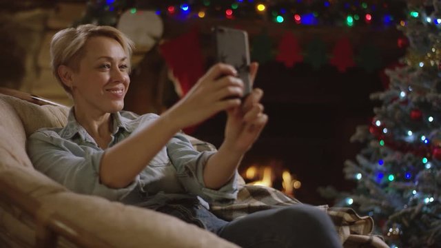 Attractive woman takes selfie in Christmas night sitting in puffchair