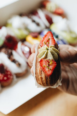 Male hand taking delicious eclair with glaze, colorful dessert