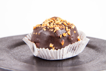 Rum ball decorated with chocolate and nuts on a black plate on a white background
