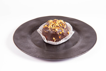 Rum ball decorated with chocolate and nuts on a black plate on a white background