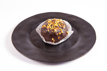 Rum ball decorated with chocolate and nuts on a black plate on a white background