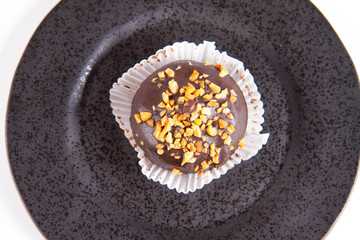 Rum ball decorated with chocolate and nuts on a black plate on a white background