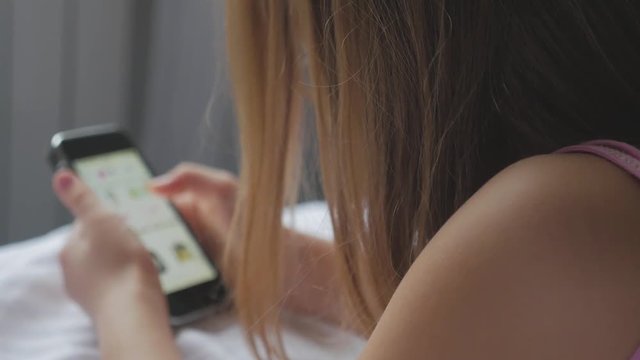 Young girl sitting on the bed and makes online shopping on a phone. Online shopping concept.