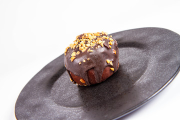 Rum ball decorated with chocolate and nuts on a black plate on a white background