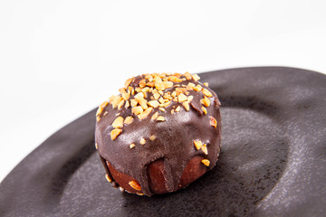 Rum ball decorated with chocolate and nuts on a black plate on a white background