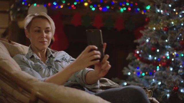 Blond woman takes selfshot on smartphone in Christmas night